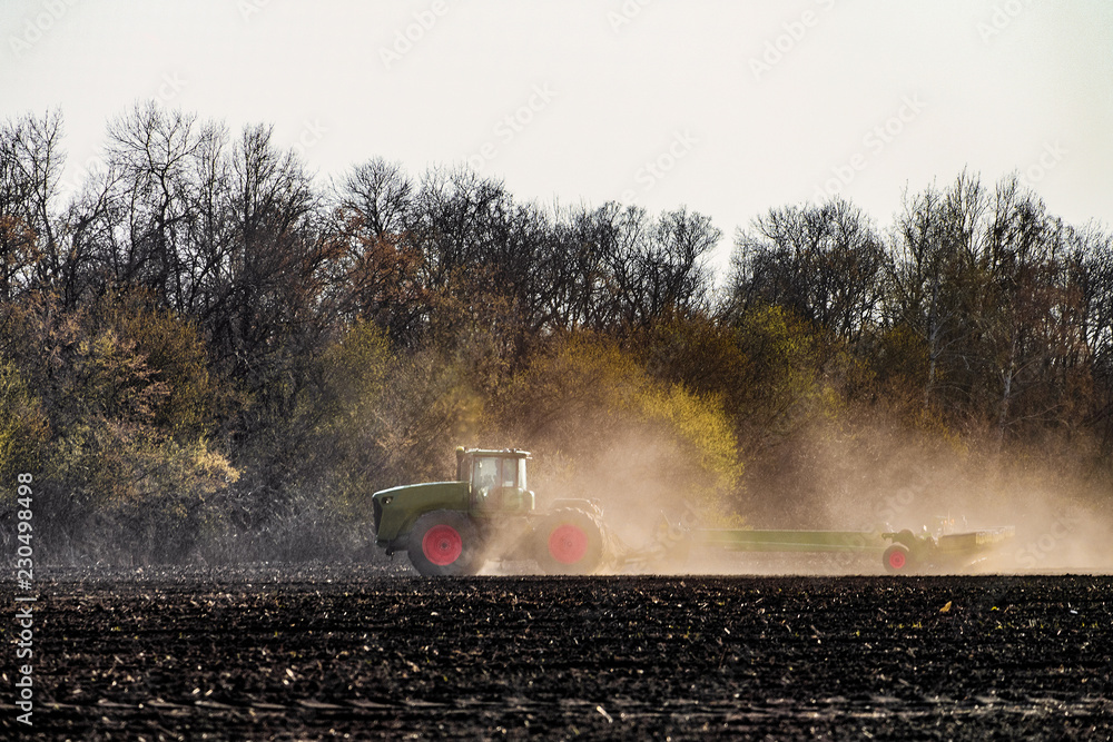 Fototapeta premium Agricultural tractor with seeder is working in the field. Agrotechnical event.