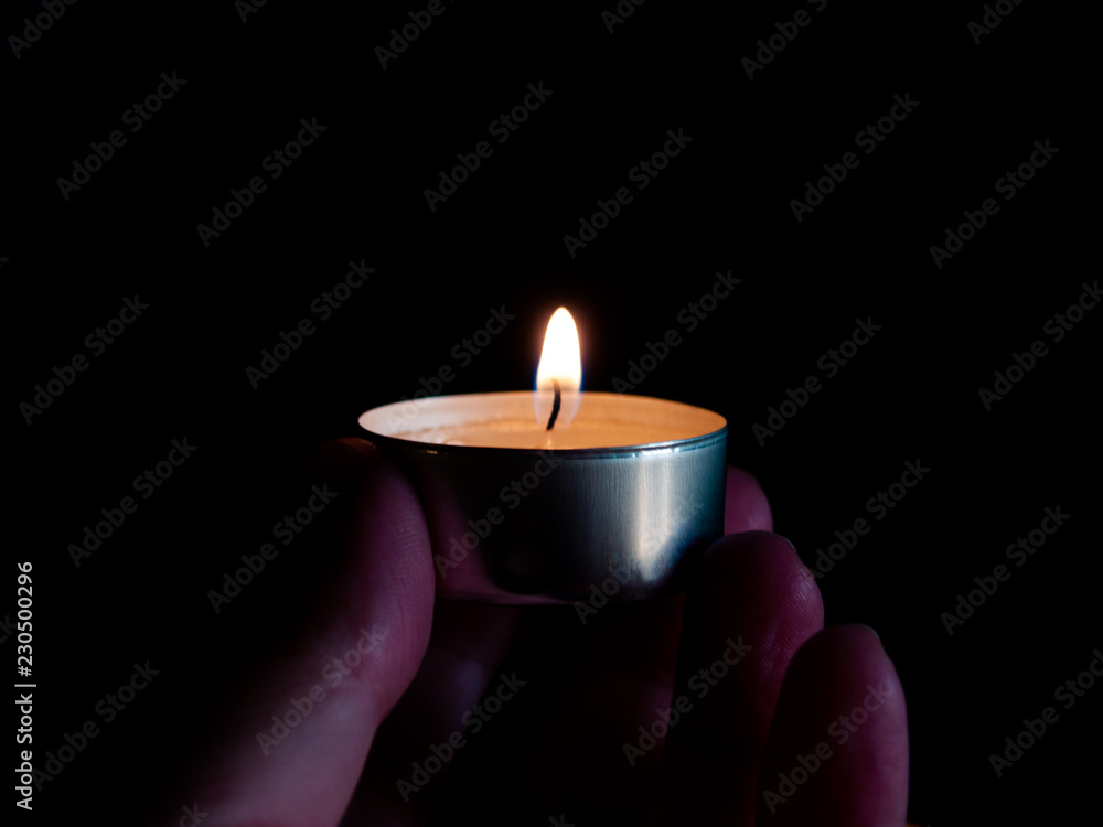 One person with a lighted candle with an orange flame in their hand and isolated on a black background One person with a lighted candle with an orange flame in their hand and isolated on a black background