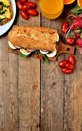 View from above of baguette sandwich with egg, arugula salad, tomatoes and radish photo