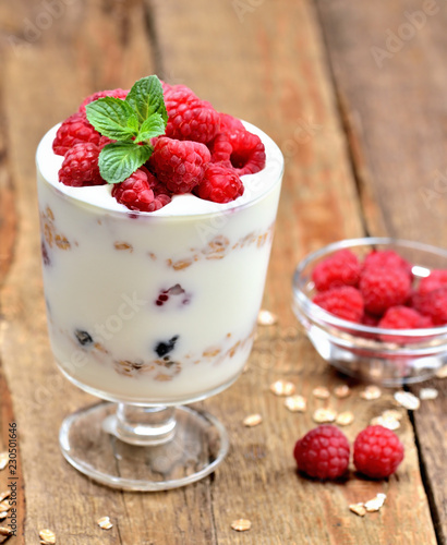 Yogurt with oatmeal and fresh raspberries in a glass and mint leaves - vertical photo