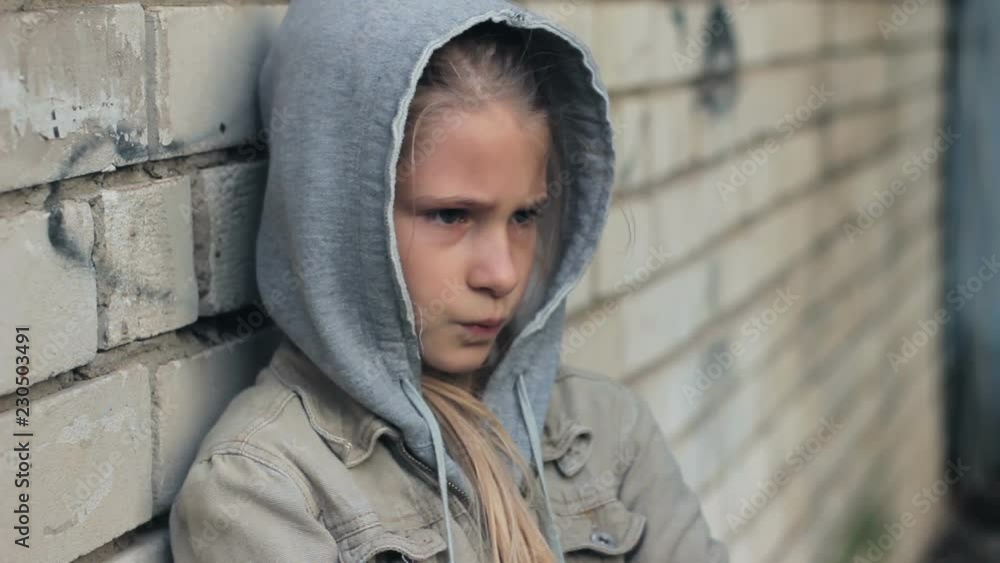 Angry offended girl child in hooded sweatshirt frowning standing leaning against grey brick wall Angry offended girl child in hooded sweatshirt frowning standing leaning against grey brick wall