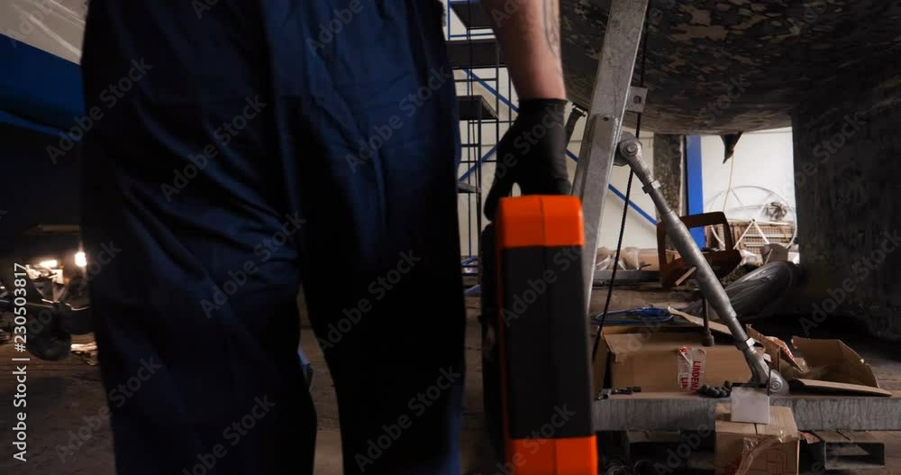 A young handsome professional engineer (mechanic) walks through the garage of the yachts with a tools in his hands. Concept of: Work start, Work class, Yacht club, Service, Garage, Tools, Work Clothes A young handsome professional engineer (mechanic) walks through the garage of the yachts with a tools in his hands. Concept of: Work start, Work class, Yacht club, Service, Garage, Tools, Work Clothes