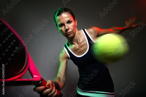 Adult fitness woman playing padel indoor. Isolated on black.