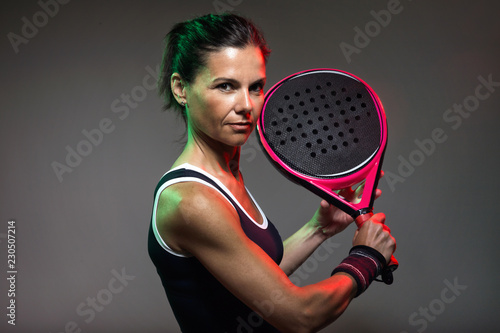 Adult fitness woman looking at camera while playing padel indoor. Isolated on black.