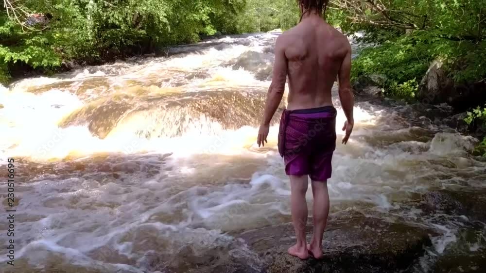Young man raises his hands at river - Muscular man filmed on a sunny day, on the side of a river, with trees in the background. Young man raises his hands at river - Muscular man filmed on a sunny day, on the side of a river, with trees in the background.