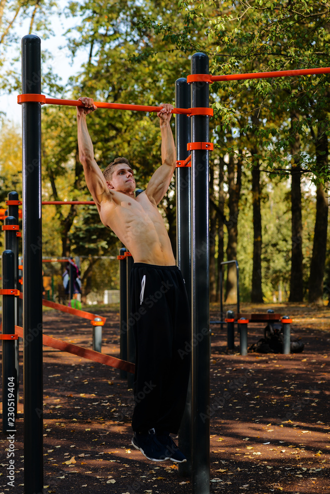 Fototapeta premium Muscular man doing pull-ups on horizontal bar