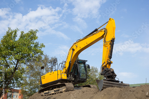 yellow excavator on the soil pile against blue sky