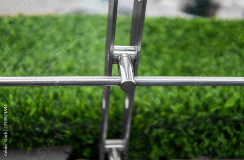 Details of fence made of stainless steel profile with an artificial raffa on the background.