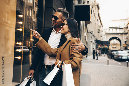 Shopping. Black Friday. Couple. Love. Man and woman with bags are looking at the shopping windows and smiling while walking down the street
