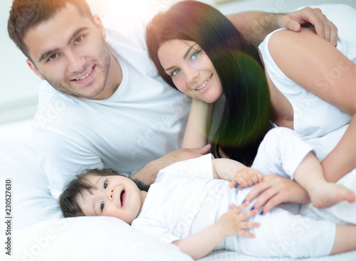 Smiling mother and father with their baby son hugging in bed
