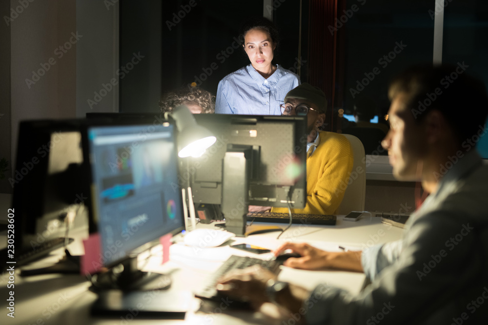 Portrait of several people working in dark office at night, focus on female manager observing process, copy space