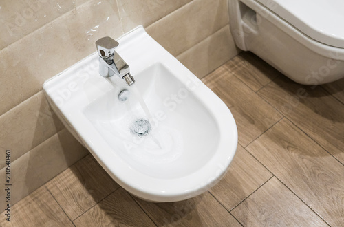 Details of white ceramic bidet with a running water in modern bathroom. photo