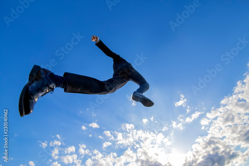 青空をバックにジャンプするスーツ姿の若いビジネスマン1人。元気・パワー・成功・挑戦イメージ
