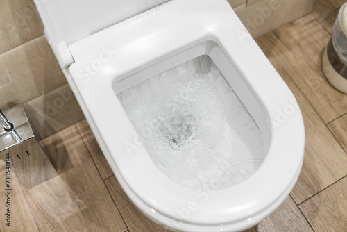 White toilet bowl in a bathroom. Closeup view of a flushing white toilet. The water swirls in the toilet bowl.