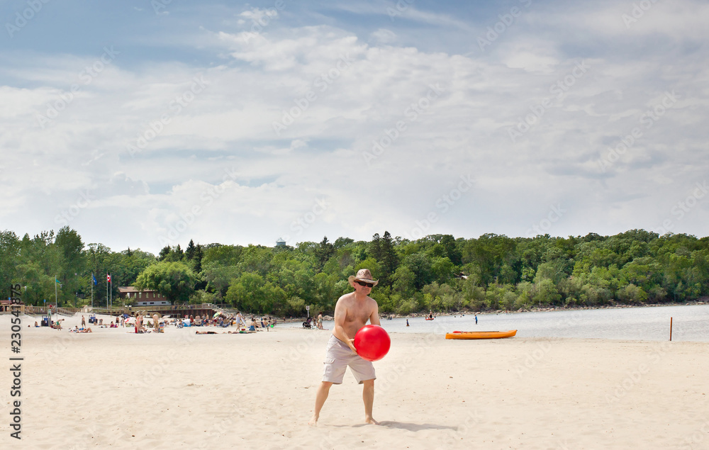 caucasian shirtless man holding red beach ball on sandy beach