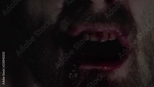 Creepy man zombie, cannibal furiously eating raw meat with frenzy. Blood drips from the mouth. Horror, halloween concept