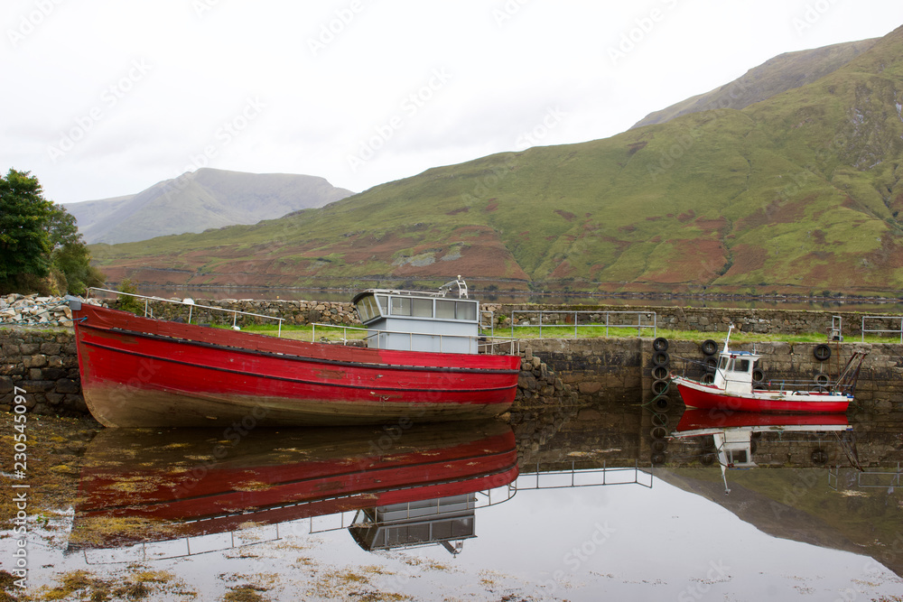 Two red fishing boats are in the foreground of this landscape view of Connemara in western Ireland
