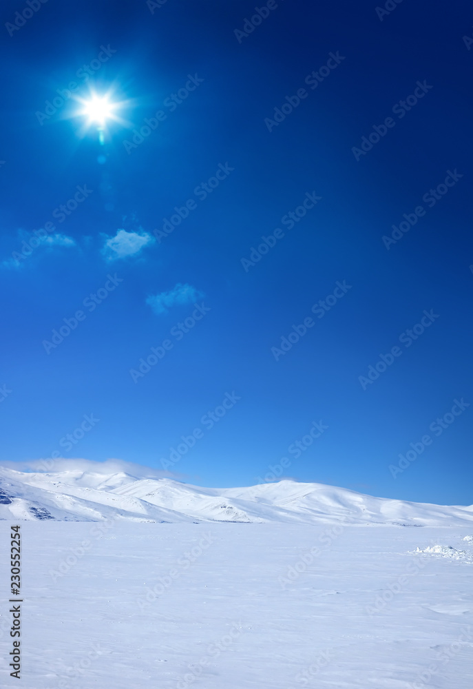 Snow covered empty frozen landscape of mountainside over blue sky with sunbeam