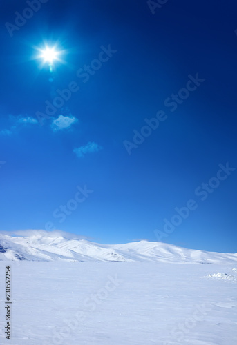 Snow covered empty frozen landscape of mountainside over blue sky with sunbeam