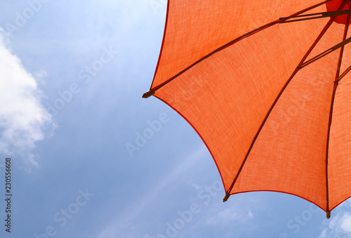 Closeup of a part of orange handmade cotton umbrella  with bright blue sky background. 