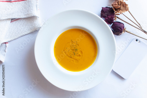 top view of delicious pumpkin potage soup for lunch with smartphone, dried flower and white background.