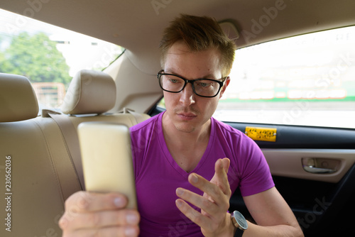 Young handsome tourist man using phone in back seat of car © Ranta Images