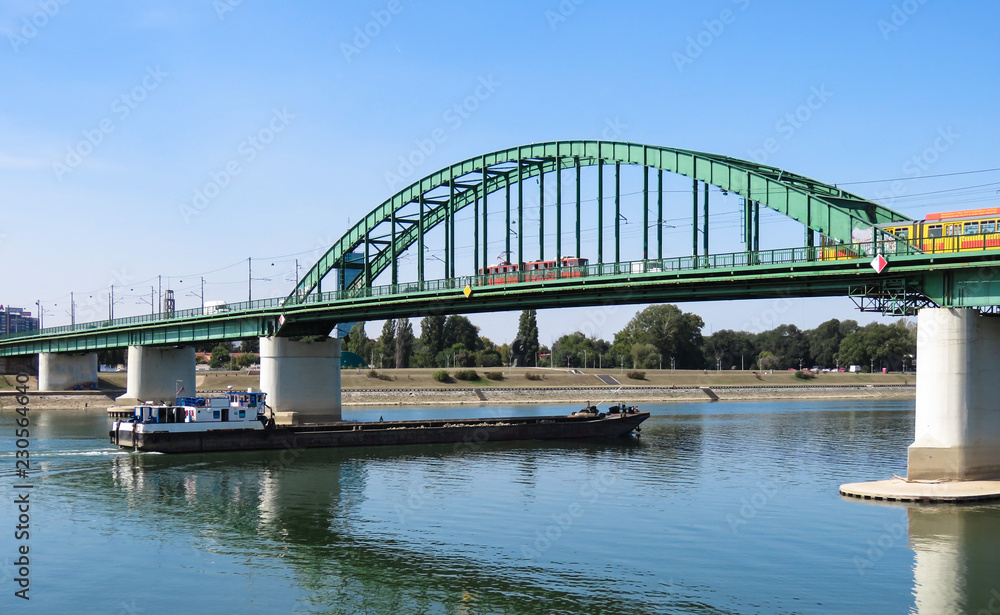 Cargo ship passing under the old railway bridge on Sava river