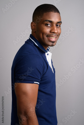 Young handsome African man wearing blue polo shirt against gray 