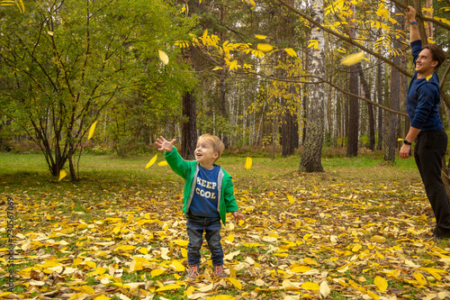 A 5 year old child rejoices at the yellow leaves falling from a tree.