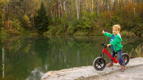 A 5-year-old boy sits on a bicycle by the pond and points to the distance.