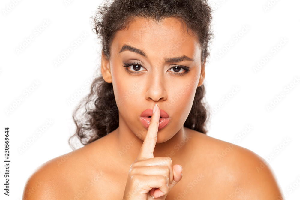 Beautiful dark skinned girl with finger over her lips on white ...