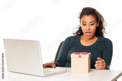 happy african woman at the desk with a laptop opens a box with a gift