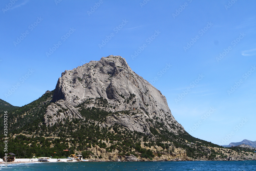 Natural landscape photo of sea and lone big mountain with bright blue sky
