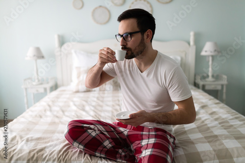 Young handsome man drinking coffee on his bed