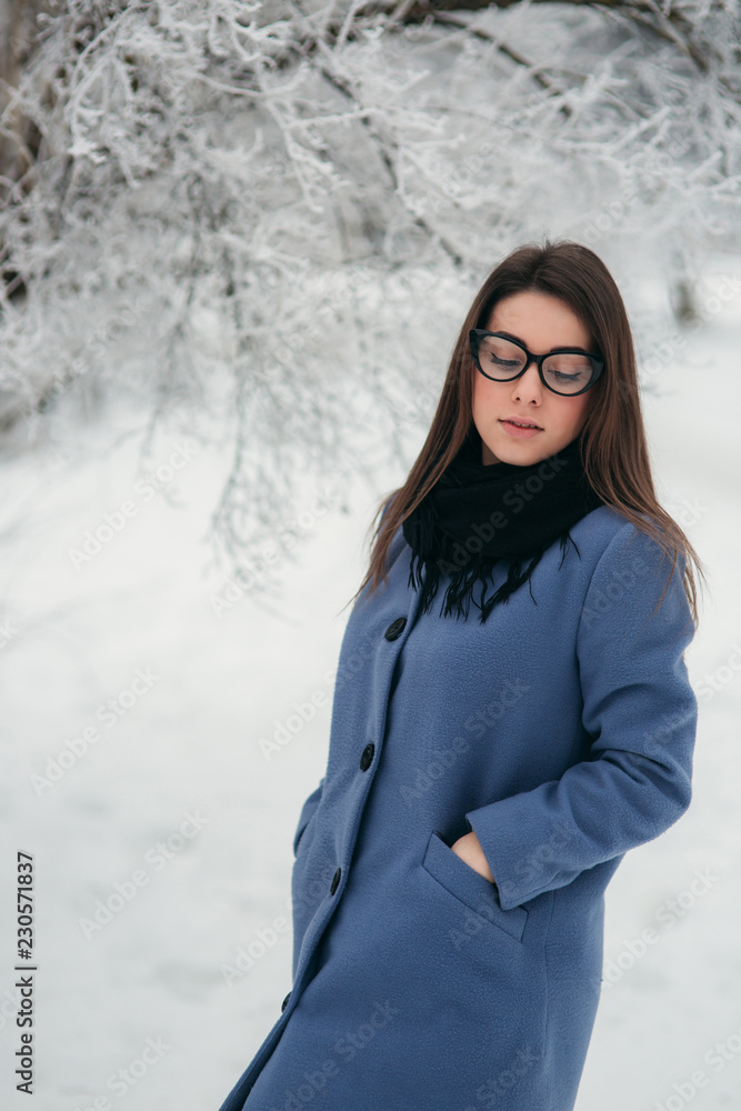 Portrait of happy young woman wearing winter hat and scarf stands next to the Christmas tree. black glasses Portrait of happy young woman wearing winter hat and scarf stands next to the Christmas tree. black glasses