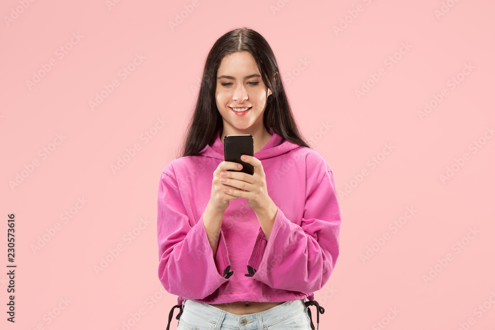 Young beautiful woman using mobile phone at studio on pink color background. Human facial emotions concept. Trendy colors Young beautiful woman using mobile phone at studio on pink color background. Human facial emotions concept. Trendy colors