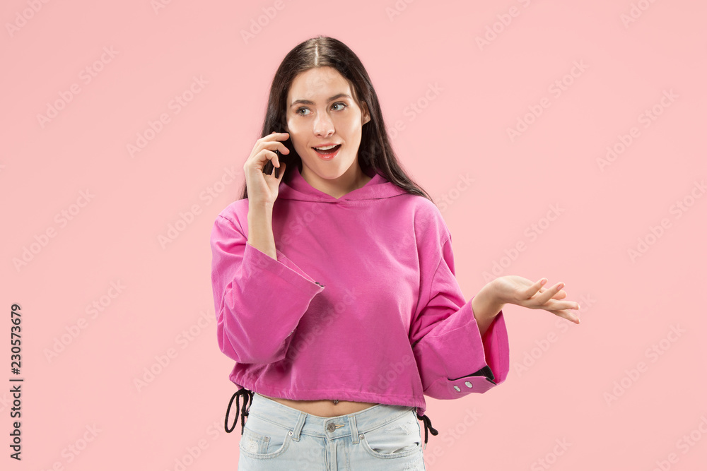 Young beautiful woman using mobile phone studio on pink color studio background. Human facial emotions concept. Trendy colors Young beautiful woman using mobile phone studio on pink color studio background. Human facial emotions concept. Trendy colors