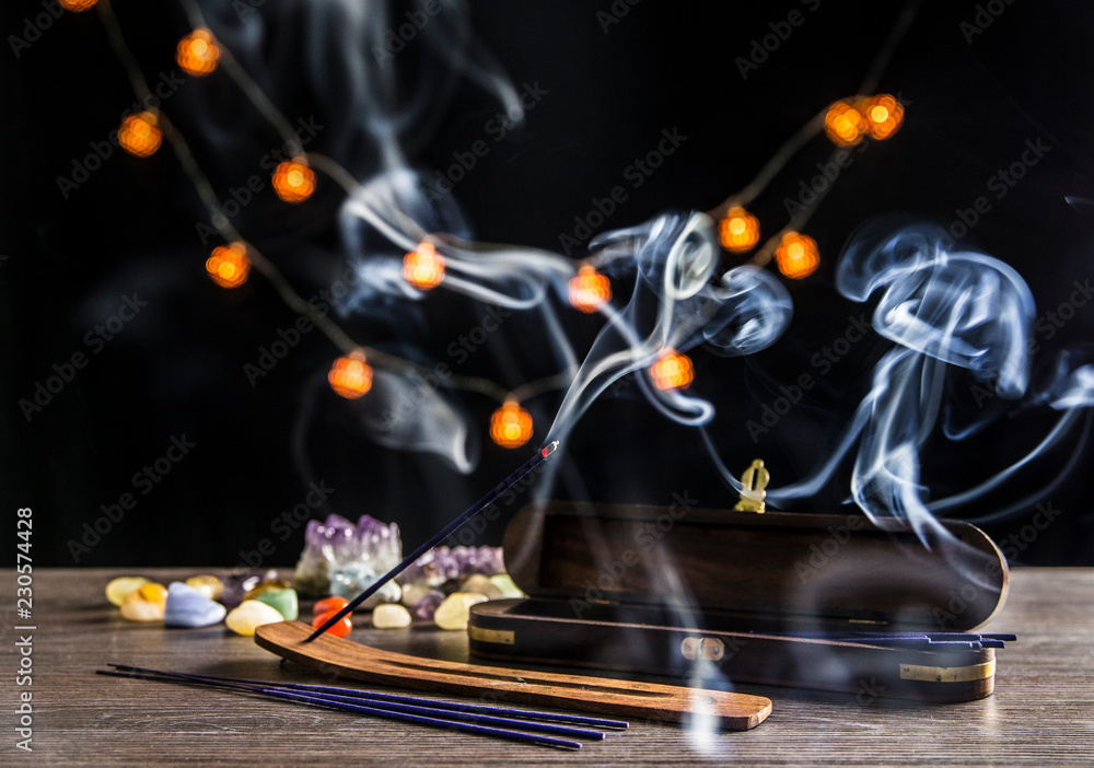 Burning incense stick and its smoke, wooden base and wooden storage box for  sticks on dark black background with semi precious stones crystals.  Spirituality concept. Stock Photo | Adobe Stock