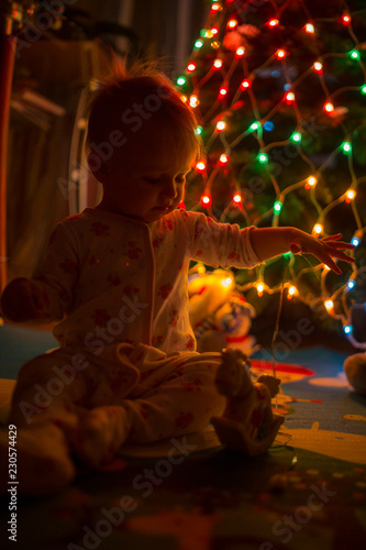 the baby is sitting under the Christmas tree