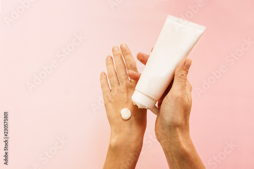 Application of moisturizer. Female hands with a white tube of cream on a pink background.