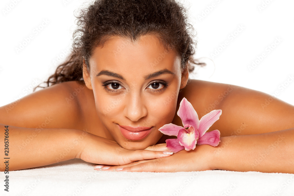 portrait of young beautiful dark-skinned woman with orchid lying on a white background