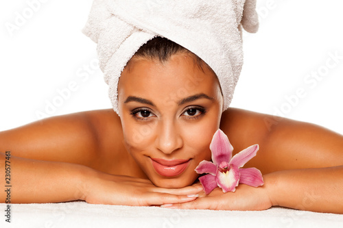 portrait of young beautiful dark-skinned woman with orchid lying on a white background