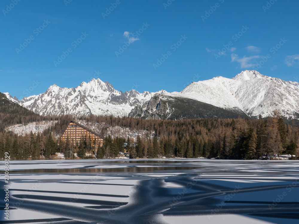 Winter in High Tatras. Winter view of frozen surface of Strbske Pleso (Tarn) with hotel and peaks of High Tatra mountains in background. Winter lake, mountains and blue sky.