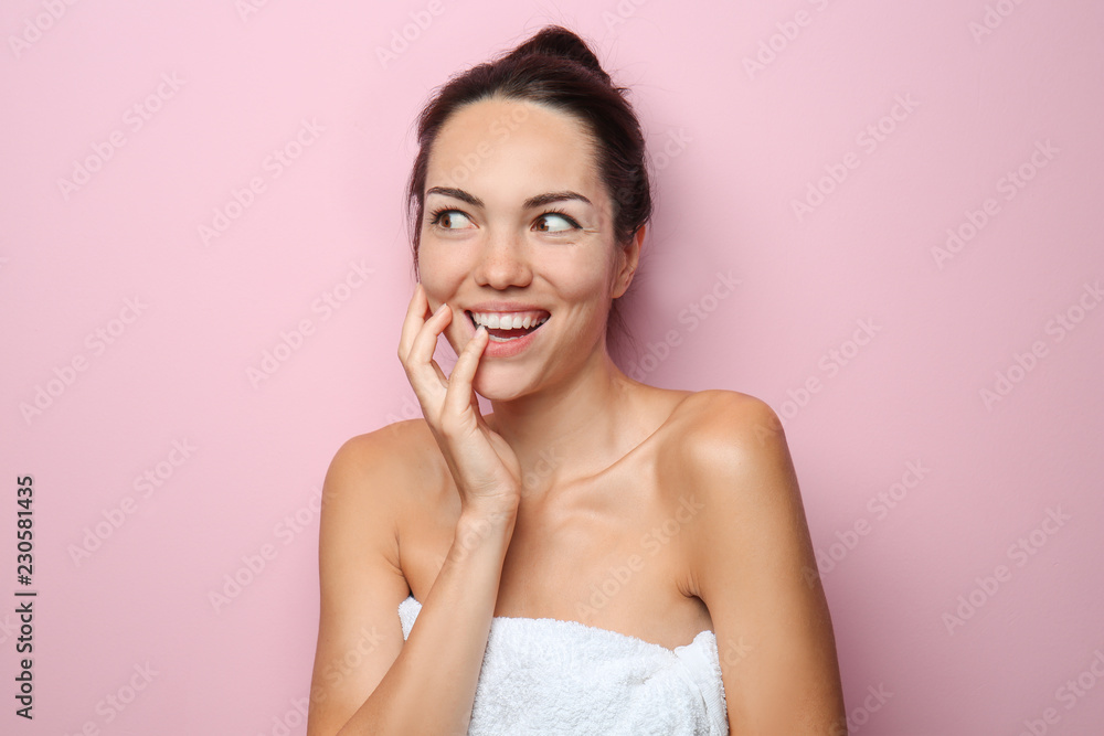 Beautiful young woman wrapped in towel on color background
