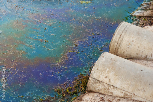 Sewer pipes at shore, stain of oil or fuel on water surface, nature pollution by toxic chemicals, dirty sea concept photo