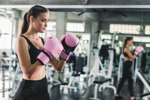 Pretty attractive Caucasian female in pink boxing gloves punching bag during workout in gym. © totojang1977