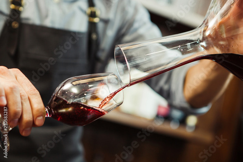 Sommelier pouring wine into glass from mixing bowl. Male waiter