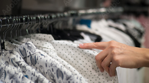 Rack with hangers in a store. Female hand holds some shirt and choose some item. Selected focus.