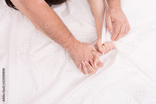 Hands of couple who making love on white crumpled sheet, focus on hands