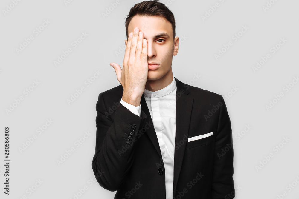 handsome young business man, male, in a classic black suit, shows poses on a gray background. handsome young business man, male, in a classic black suit, shows poses on a gray background.